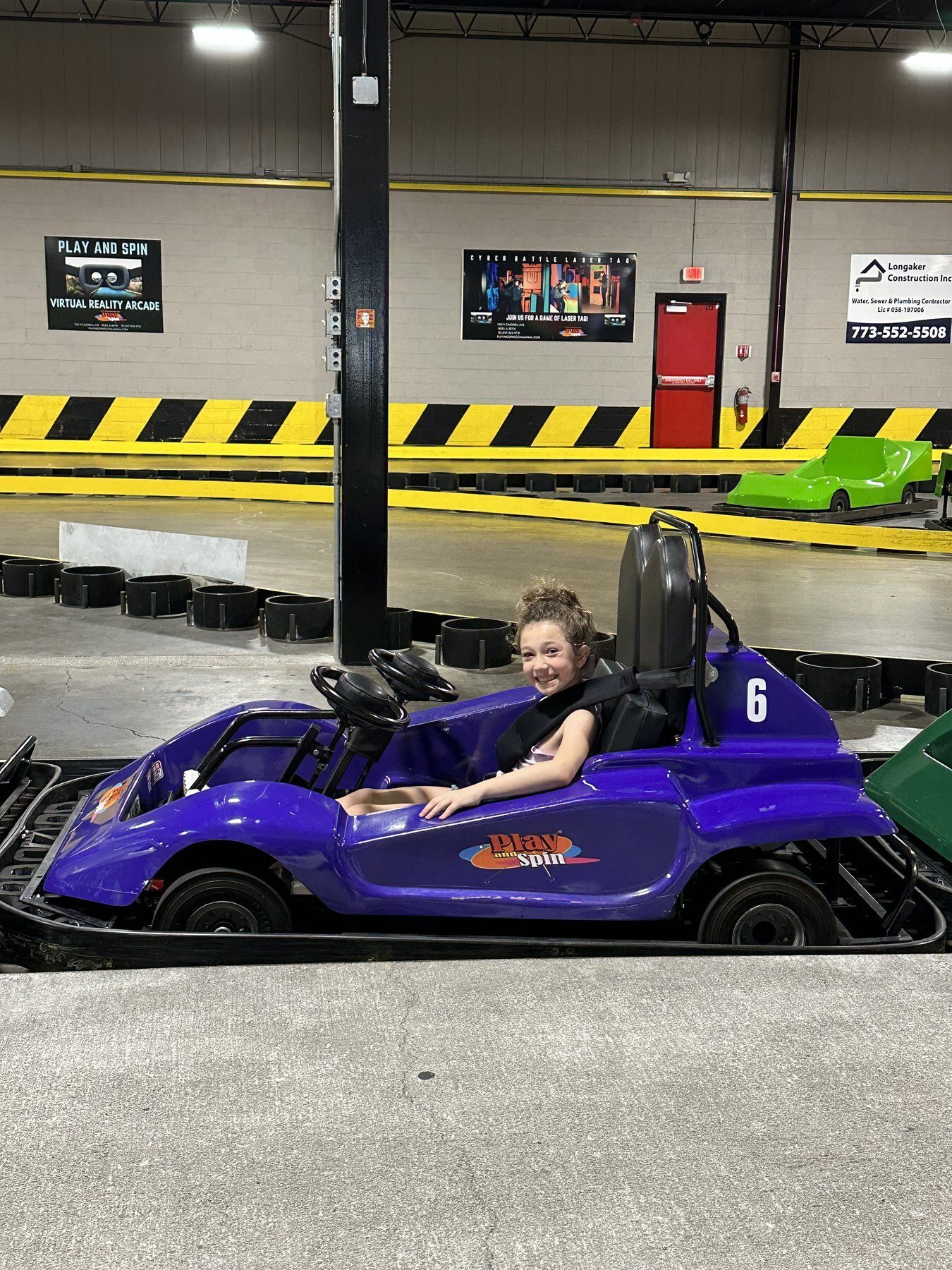 Girl smiling in Play and Spin branded go-kart on the indoor racing track in Niles Illinois
