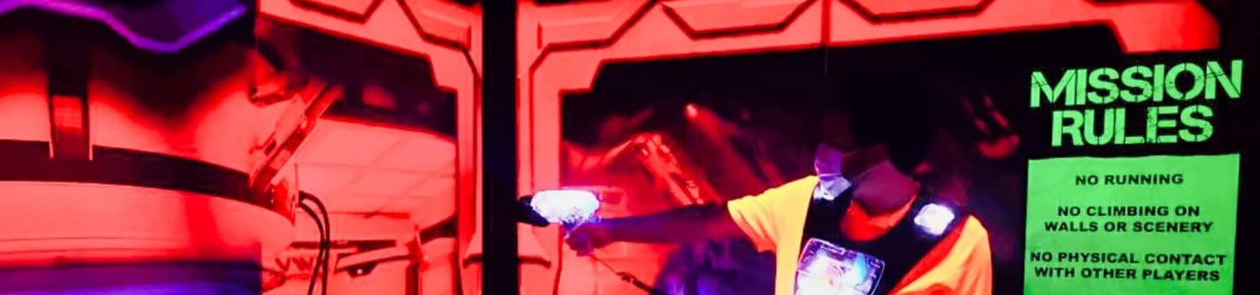 Player firing phaser in the Cyber Battle Laser Tag arena at Play and Spin in Niles with Mission Rules sign